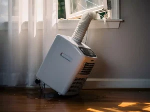 Draagbare mobiele airco scheef tegen woonkamermuur, geknikte koelslang door raamkier, condenswater op vloer.