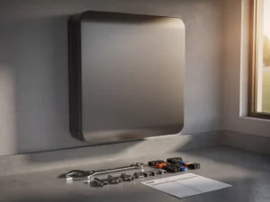 Thuisbatterij gemonteerd op garagemuur met installatiegereedschap, kabelconnectoren en factuurblad op betonvloer.